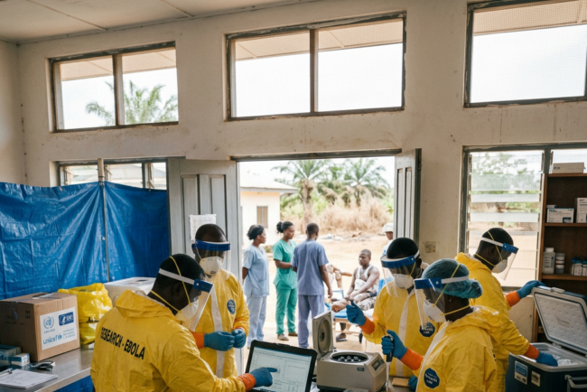 Healthcare workers in yellow protective suits and face shields working with laboratory equipment in an Ebola research facility